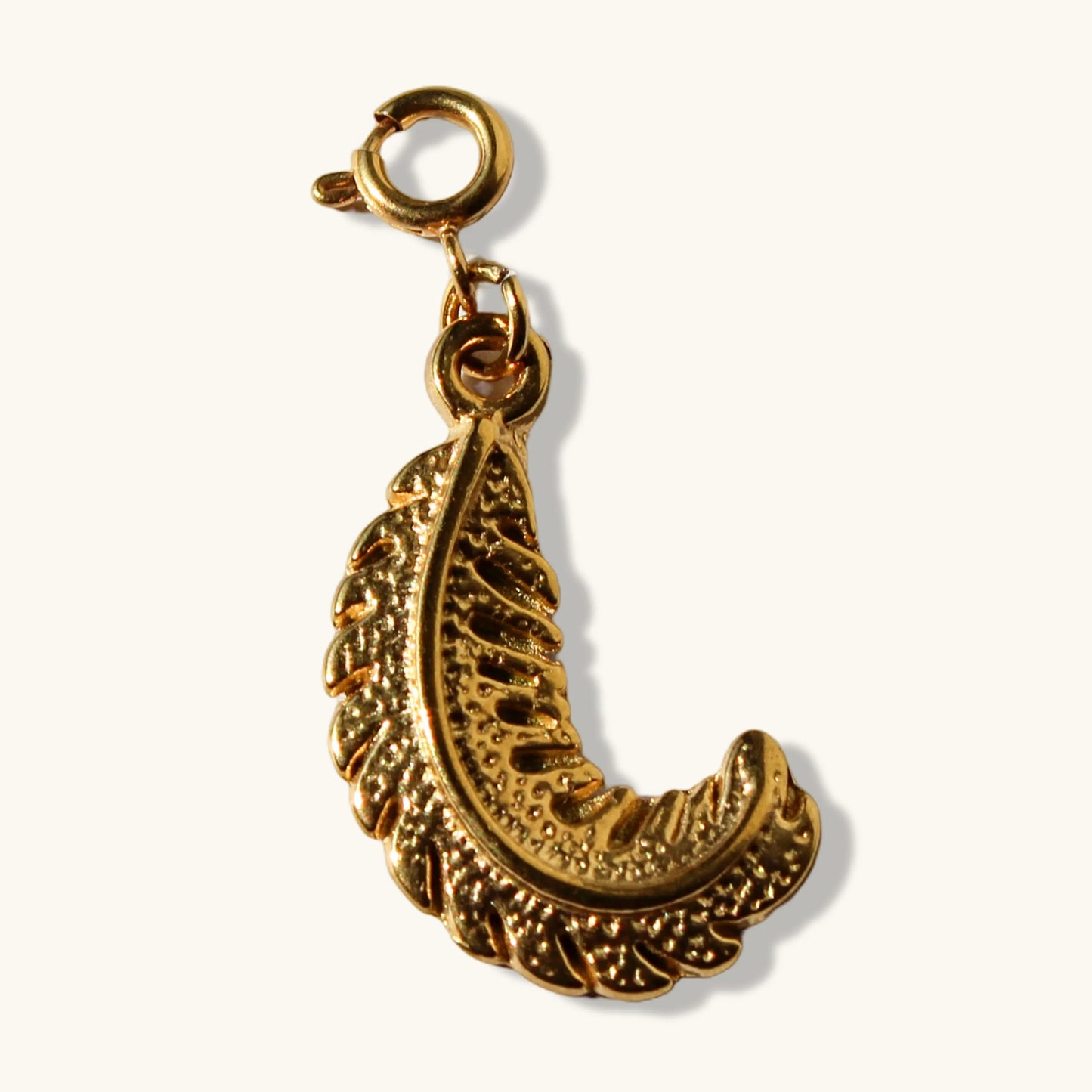 Gold paisley shaped jewelry charm with intricate texture on white background