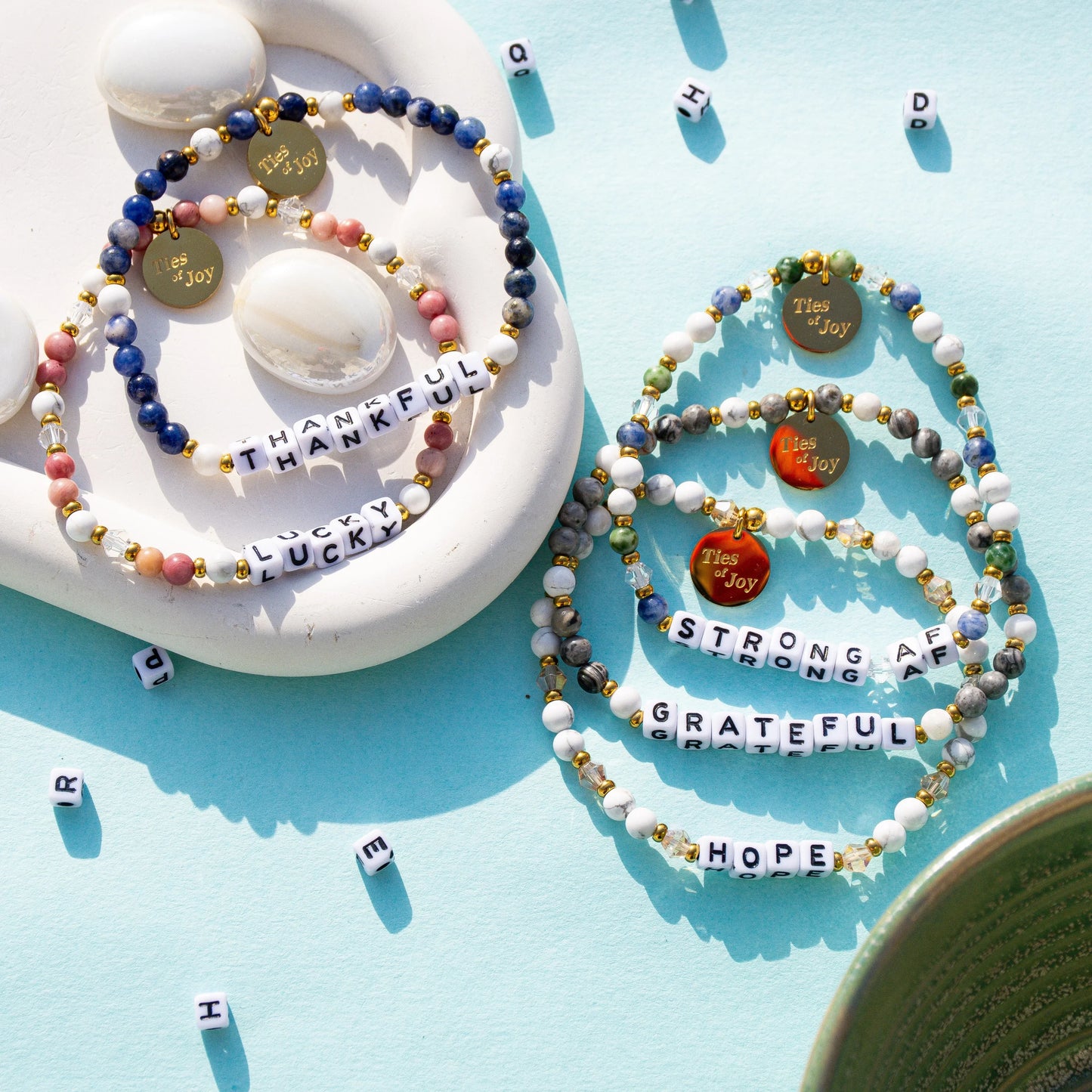 Colorful beaded bracelets with uplifting words like thankful, lucky, strong, and grateful on a blue background.