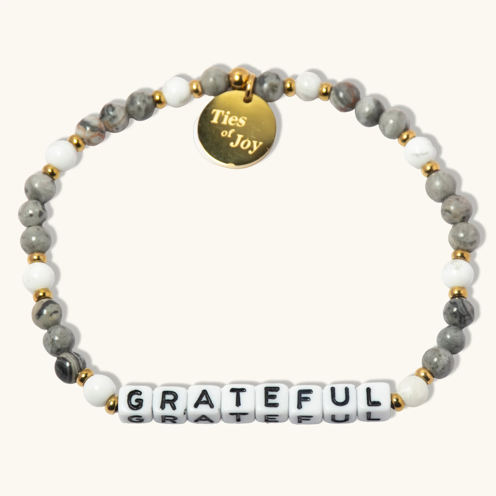 Gray and white beaded bracelet with gold charm reading 'Ties of Joy' and 'GRATEFUL' letter beads.