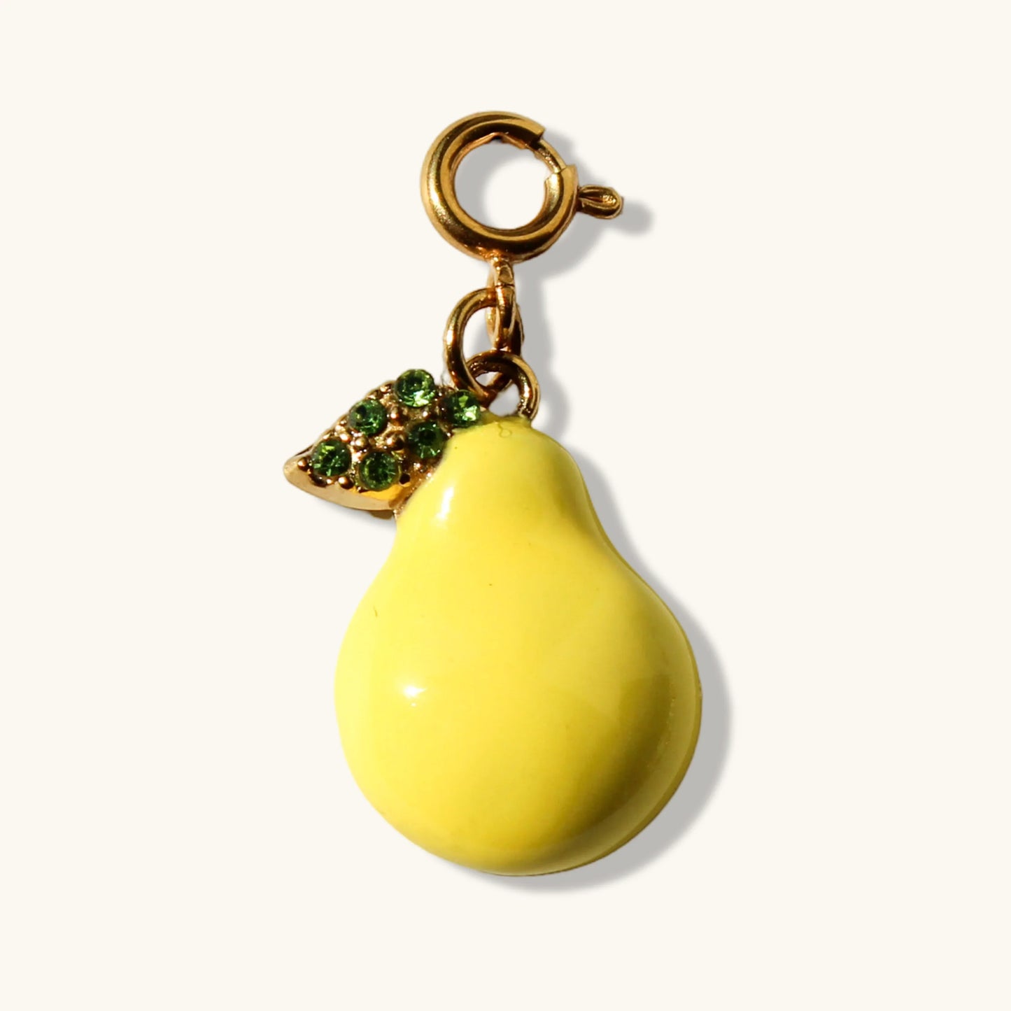 Yellow pear charm pendant with gold clasp and green rhinestone leaf on white background