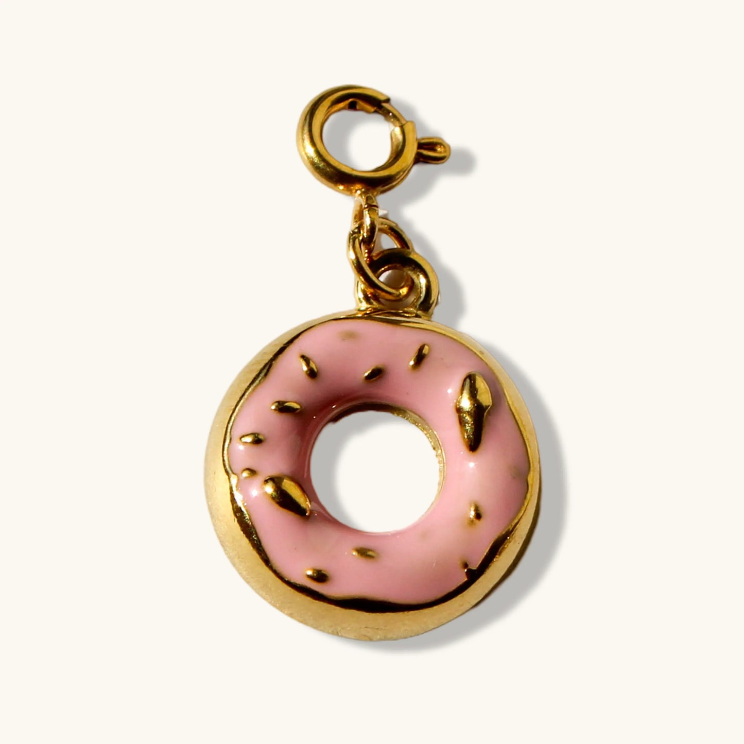Gold donut charm with pink enamel and sprinkles on a cream background