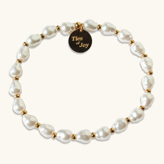 Pearl beaded bracelet with gold accents and Ties of Joy round charm on a light background