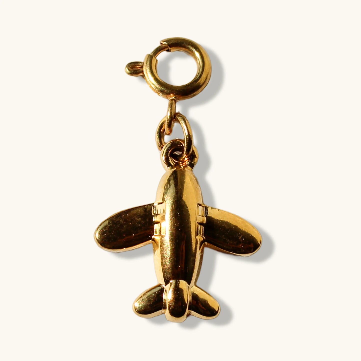 Gold airplane charm pendant with clasp on a plain light background