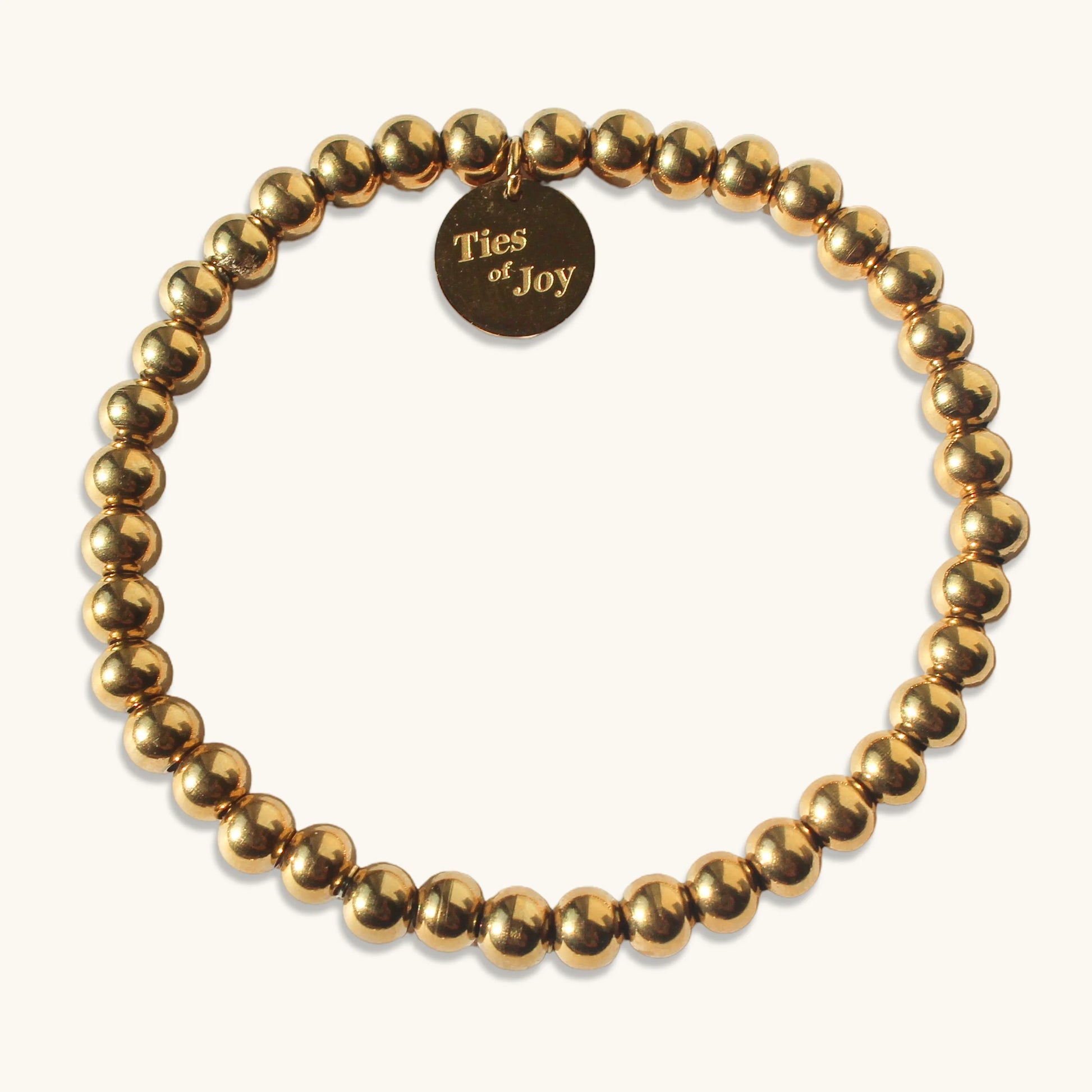 Gold beaded bracelet with round Ties of Joy charm on a light background