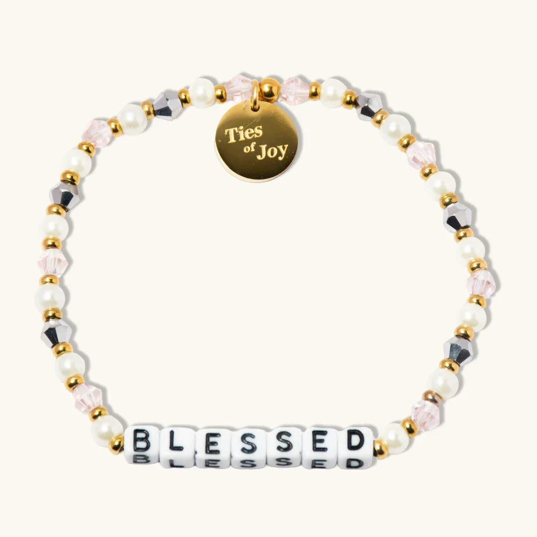 Blessed beaded bracelet with pearls, gold accents, and Ties of Joy charm on cream background