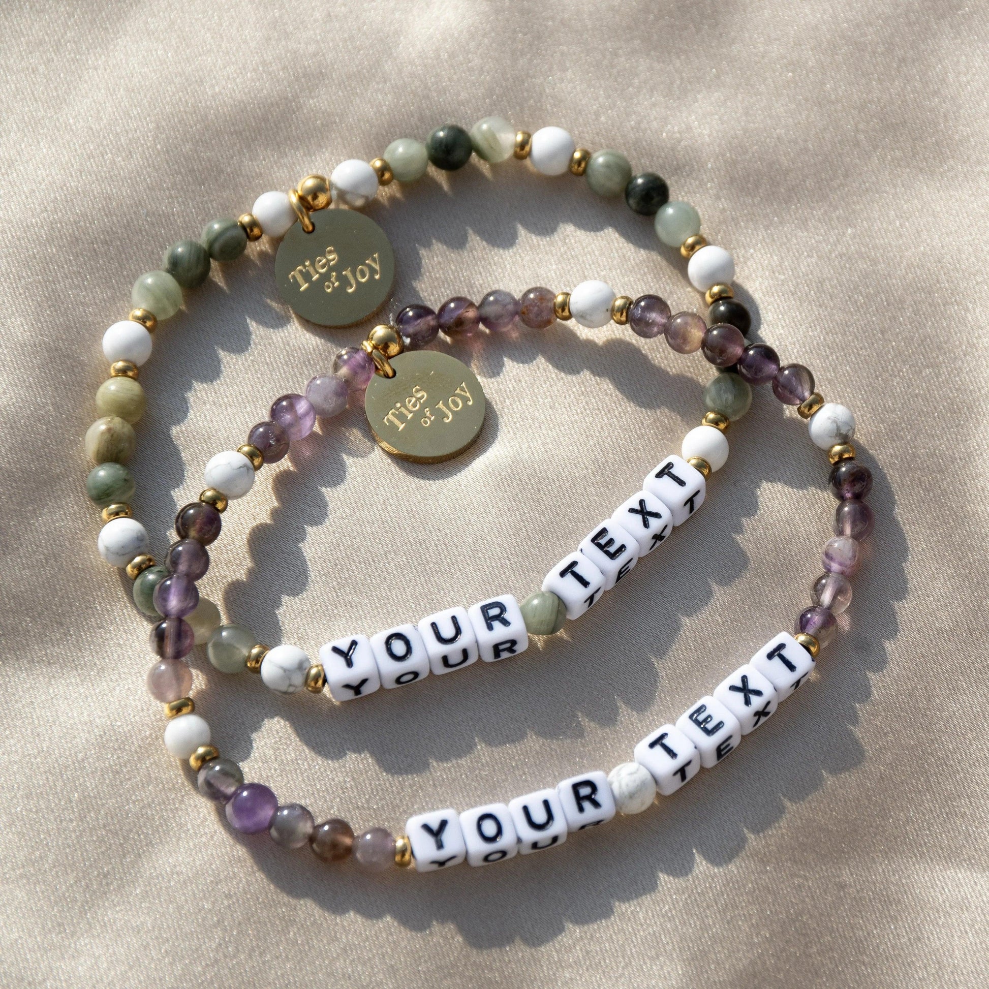 Custom beaded bracelets with 'YOUR TEXT' letter beads and Ties of Joy gold tags on fabric