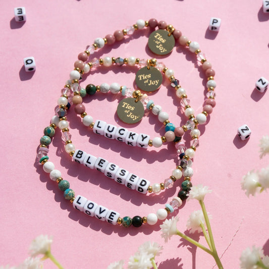 Beaded charm bracelets with words Lucky, Blessed, Love on pink background, Ties of Joy tags